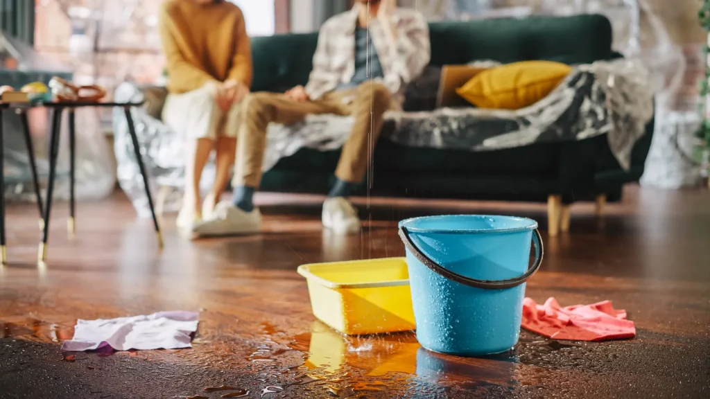 Water damage in a living room from a burst pipe, with buckets catching drips